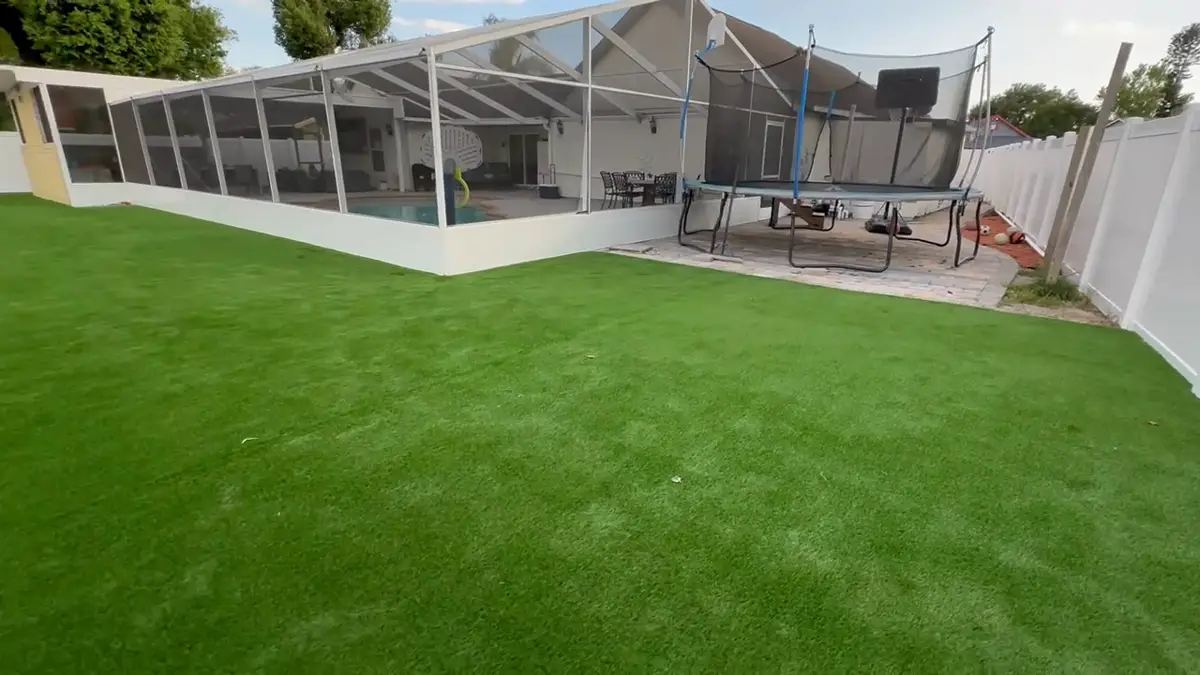 Artificial turf installed in a backyard with a white fence and pool enclosure